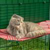 Chat couché nettoyant sa patte sur une étagère extérieure rouge et imperméable pour chat dans un catio