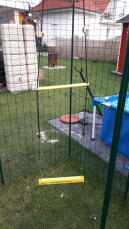 Une balançoire à poulet jaune placée dans un grand enclos
