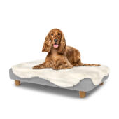 Chien assis sur un lit pour chien de taille moyenne Topology avec surmatelas en peau de mouton et pieds ronds en bois