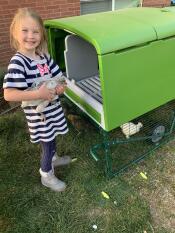 Une petite fille tenant un poulet à l'extérieur d'un Eglu.