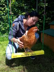 Une femme tenant un poulet brun sur une balançoire à poulet jaune dans un walk in run