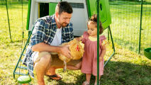 Homme avec sa fille tenant une poule dans un poulailler