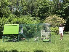 Une jeune fille dans un jardin avec un poulailler vert Cube et un parcours attenant