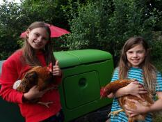 Deux filles tenant des poulets à côté de leur poulailler