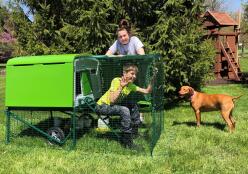 Une dame, un garçon, un chien et leur Omlet vert Eglu Cube grand poulailler et parcours pour poules