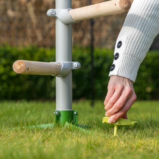 La femme fixe le système de perchoir universel pour poules sur le terrain à l'aide des chevilles à vis Omlet.