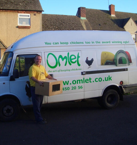 Un livreur à côté d'une camionnette de la marque Omlet transportant une boîte de poulets