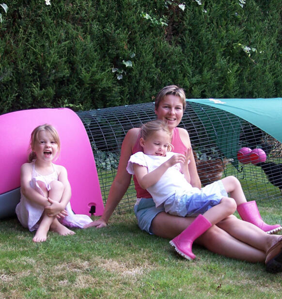 Une famille assise à côté d'un poulailler rose Eglu 