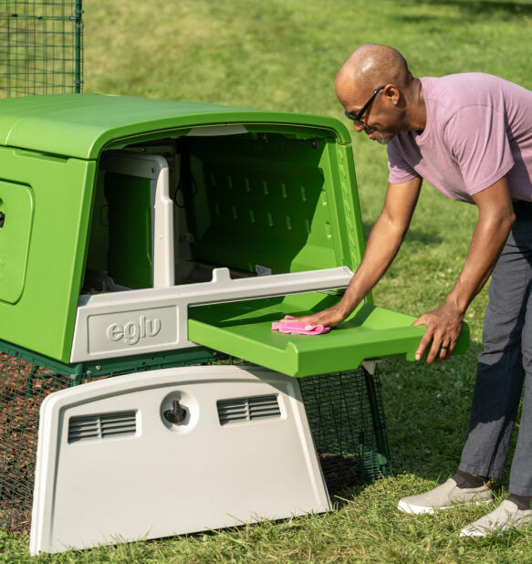 Un homme qui nettoie le plateau à déjections du poulailler Eglu Cube.