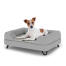 Chien assis sur un petit lit pour chien Topology avec traversin gris et pieds en épingle à cheveux en métal noir Chien assis sur un petit lit pour chien Topology avec traversin gris et pieds en épingle à cheveux en métal noir