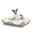 Chien assis sur un petit lit pour chien Topology avec une couverture en peau de mouton et des pieds ronds en bois. Chien assis sur un petit lit pour chien Topology avec une couverture en peau de mouton et des pieds ronds en bois.