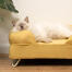 Mignon chat blanc en peluche qui dort sur un lit à traversin jaune moelleux avec pieds en épingle à cheveux blancs