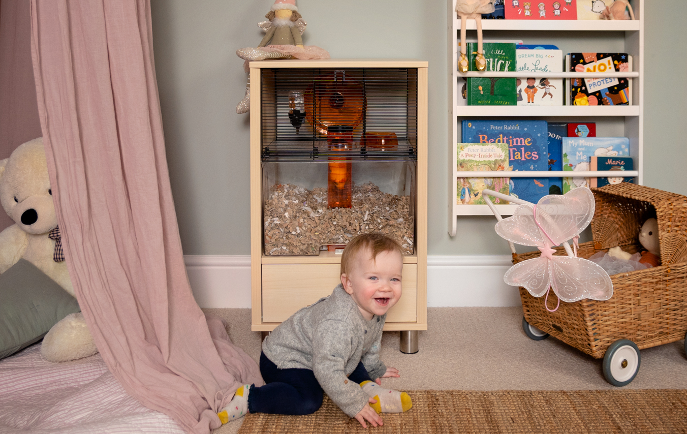 Jeune enfant qui joue dans sa chambre avec une cage pour hamster en arrière-plan