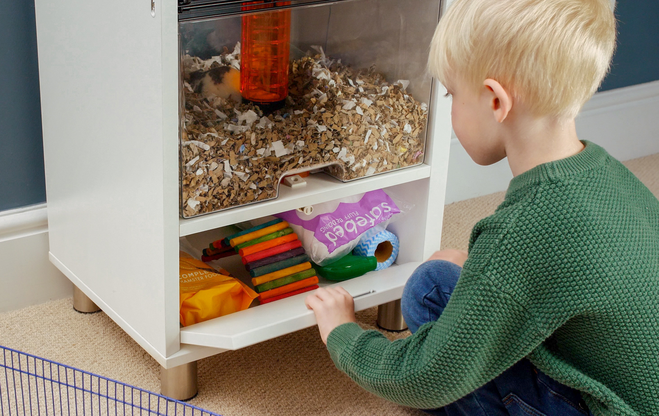 Enfant qui range la litière du hamster dans l’espace de rangement de la cage Qute pour hamsters